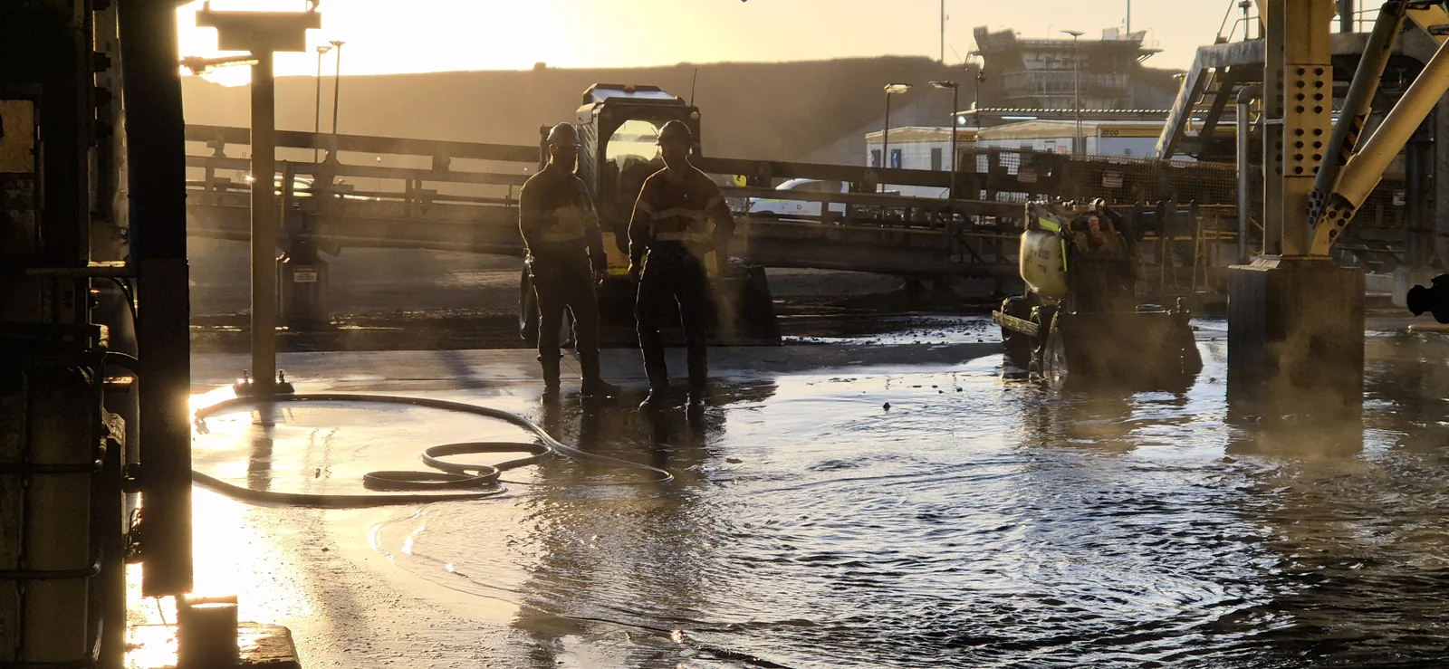 Crew hosing down a coal preparation plant floor at sunrise