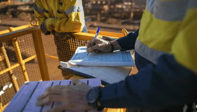 Worker in hi-vis filling out a checklist on a plant walkway